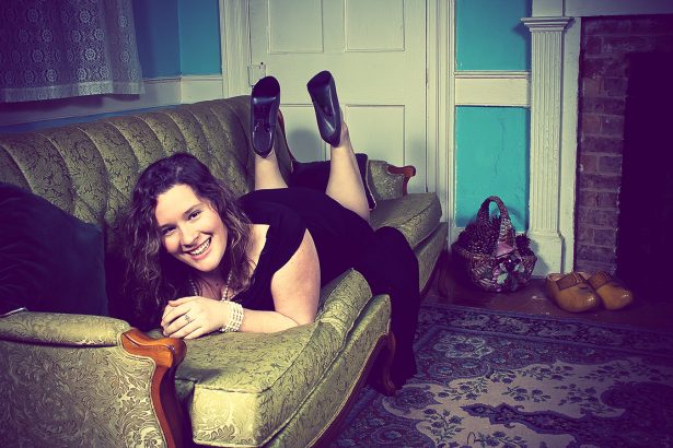 photo of a smiling woman in black dress posing on a green couch