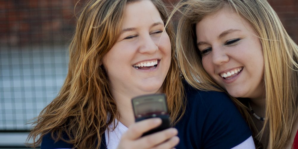 photo of two women looking at a cell phone and sharing a laugh