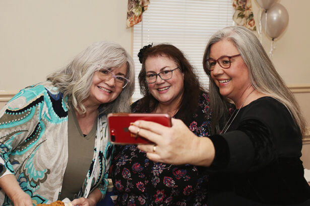 three women pose for a selfie with an iPhone in the foreground
