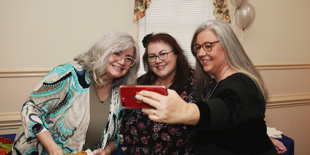 three women pose for a selfie with an iPhone in the foreground