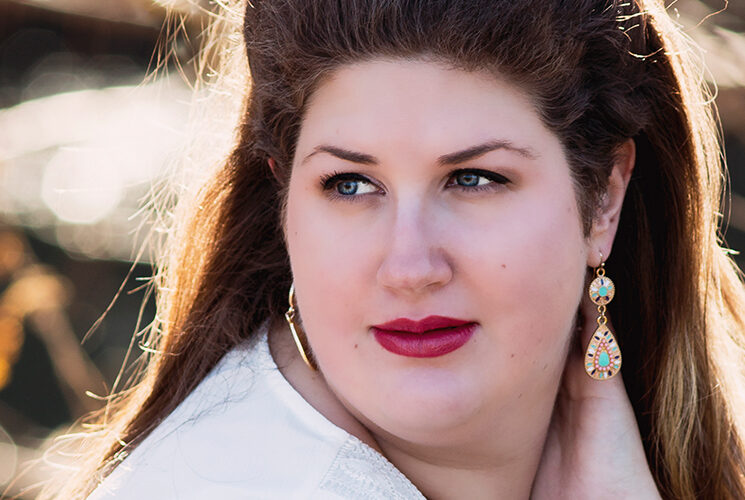 Portrait of a woman outdoors in warm autumn light, looking to the side with soft expression and colorful earrings.