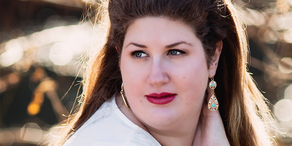 Portrait of a woman outdoors in warm autumn light, looking to the side with soft expression and colorful earrings.