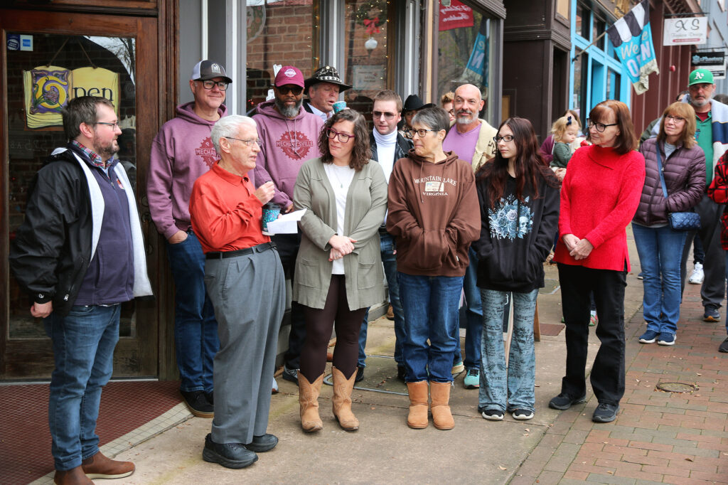 City Councilman Dr. Gary Miller speaks to a gathered crowd outside The Dogeared Page Bookshop in Danville, Virginia, during the store’s grand reopening, standing with the new owners and community members.