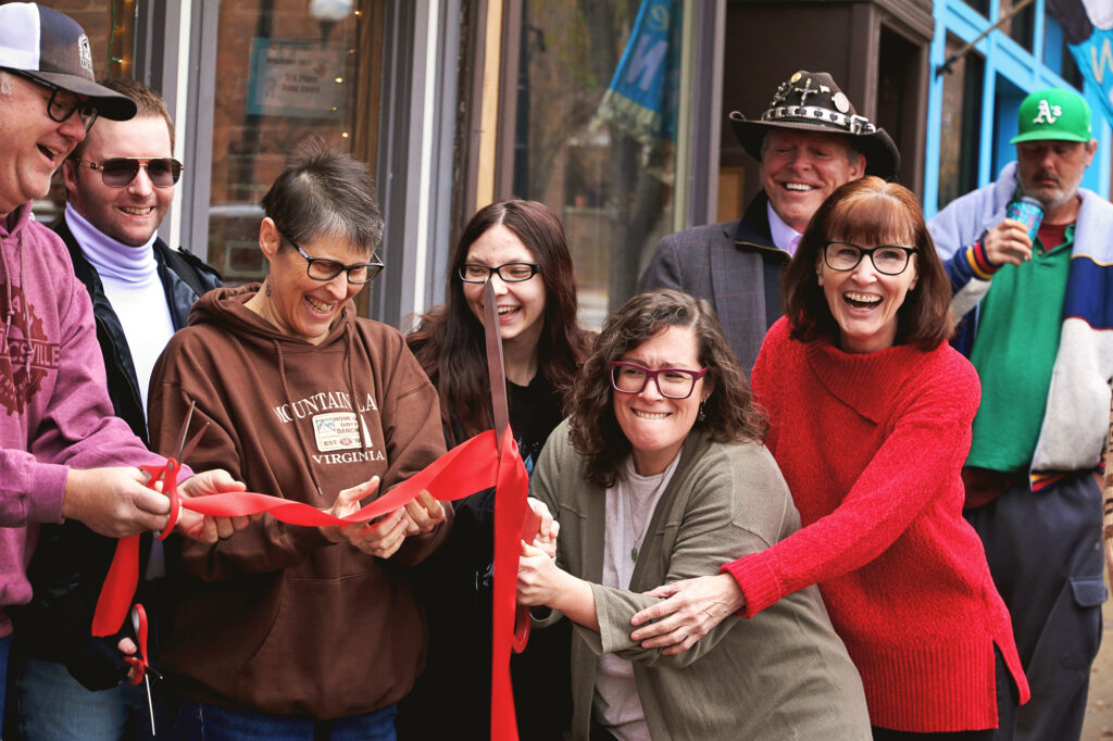 Katelyn Murray struggles to cut the red ribbon with oversized ceremonial scissors during the grand reopening of The Dogeared Page Bookshop in Danville, Virginia, while her mother and co-owner Maryann Howerton laugh and try to assist.