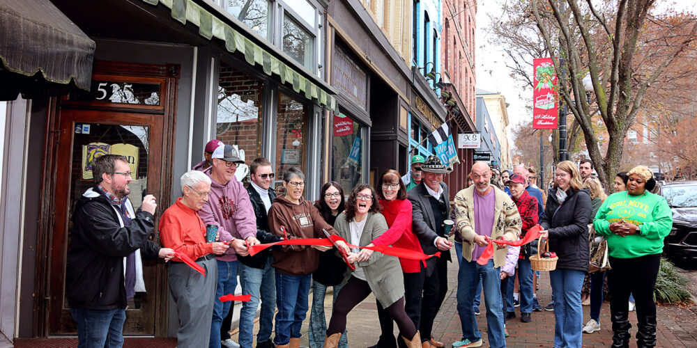 The new owners of The Dogeared Page Bookshop cut a red ribbon outside the storefront on Main Street in Danville, Virginia, as a cheerful crowd of community members looks on during the grand reopening ceremony.