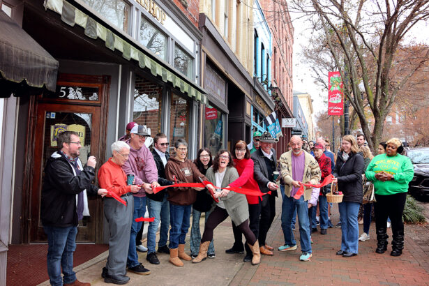 The new owners of The Dogeared Page Bookshop cut a red ribbon outside the storefront on Main Street in Danville, Virginia, as a cheerful crowd of community members looks on during the grand reopening ceremony.