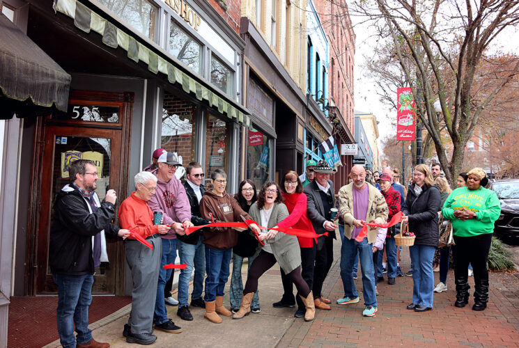 The new owners of The Dogeared Page Bookshop cut a red ribbon outside the storefront on Main Street in Danville, Virginia, as a cheerful crowd of community members looks on during the grand reopening ceremony.